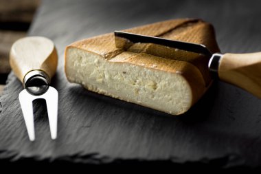 Füme keçi peyniri ile sıkışmış bıçak ve çatal siyah taş tahta üzerinde yığın