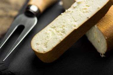 Yığın füme keçi peyniri ve çatal, siyah taş kurulu ile kalın dilim kesilmiş kapat