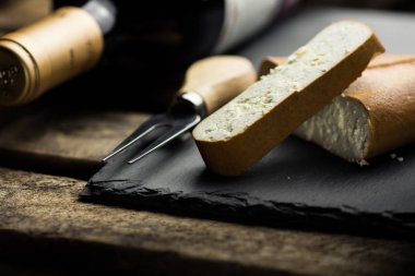 Yığın ve kalın dilim füme Keçi peynir siyah taş masa, şişe şarap, gurme yemek çatalı ile kesmek