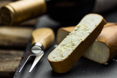 Yığın ve kalın füme keçi peyniri çatal tahtada siyah taş, şişe şarap ile dilim kesilmiş