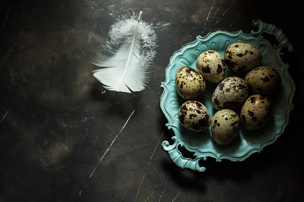 Huevos de codorniz en placa azul vintage, pluma blanca, sobre fondo de hormigón rayado negro, concepto de Pascua, minimalista — Foto de Stock