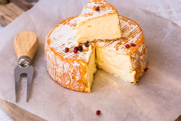 Vista superior de rebanada cortada de queso blando francés o alemán con corteza de naranja con moho, textura cremosa, granos de pimiento rojo, tenedor, sobre papel pergamino —  Fotos de Stock