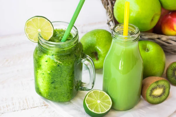 Suco de frutas e ervas verdes em garrafa, smoothie vegetal na caneca com palha, maçãs na cesta, limão, kiwi, ao ar livre, primavera de verão — Fotografia de Stock