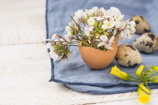 Decoración interior de Pascua, ramo de flores blancas amarillas en cáscara de huevo, huevos de codorniz, servilleta azul en la mesa de madera — Foto de Stock