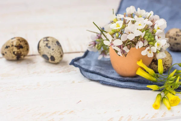 Bouquet of white yellow flowers in eggshell, quail eggs, blue napkin on wood table, Easter interior decoration — Stock Photo, Image