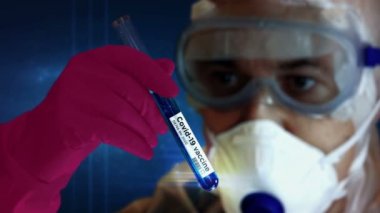 Coronavirus Covid-19 aşı araması. Koruyucu gözlüklü ve maskeli bir bilim adamı eldiven takmış test tüpüyle. Bilim, biyoloji, sağlık, tıbbi, virüs araştırması, salgın ve salgın hastalık kavramı.