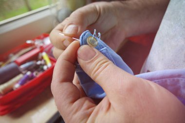 İğne ve iplik terzinin elinde. Gömlek düğmesini elle dikiyorum. El yapımı iş.