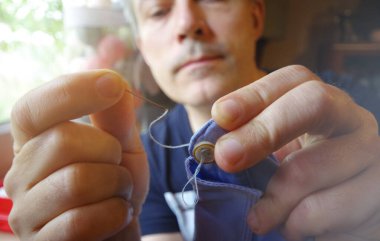 Elinde iğne ve iplik olan terzi. El yapımı iş. Gömlek düğmesini elle dikiyorum. El işi..