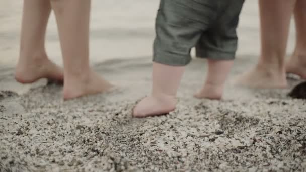 Bebé primeros pasos en la arena whit padres. primer plano de los pies — Vídeo de stock