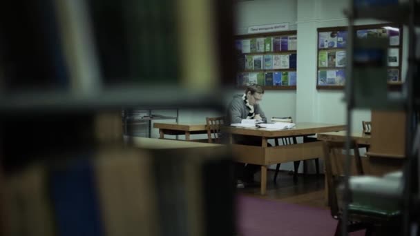 Студент читает книгу в библиотеке, сидит за столом, двигает камеру — стоковое видео
