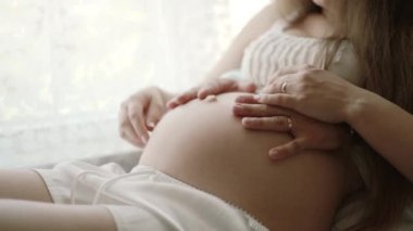 Hamile bir kadın ve kocası yatakta evde oturan ve okşayarak göbek