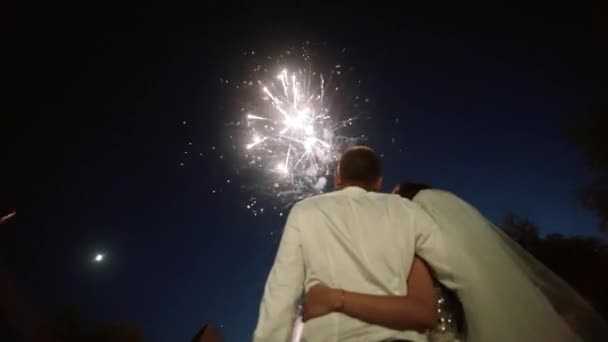 La novia y el novio se quedan atrás y miran los fuegos artificiales en la noche — Vídeo de stock