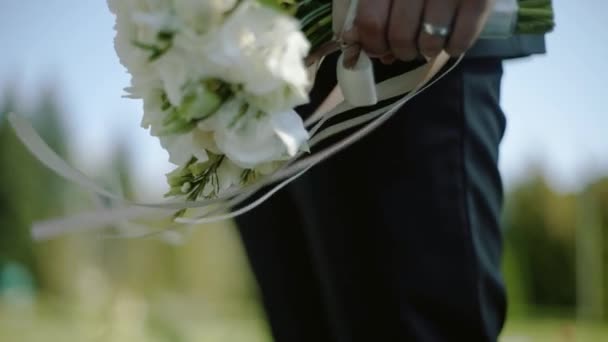 O noivo segura um buquê com fitas no vento — Vídeo de Stock
