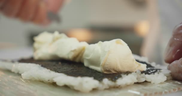 Processus de fabrication des sushis. apporter du fromage sur la pièce à usiner pour rouler des sushis Empilement d'ingrédients pour les rouleaux de sushis riz, concombres, fromage feta, saumon Mouvement lent. Gros plan — Video