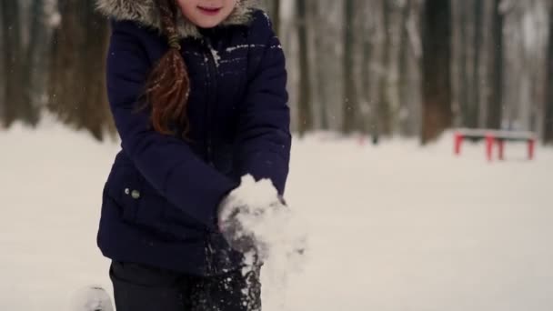 Dziecko bawię się w zimie w park rzucam śnieg. rzuca płatki śniegu i uśmiecha się w zimowym parku. Powolny ruch Zamknij — Wideo stockowe