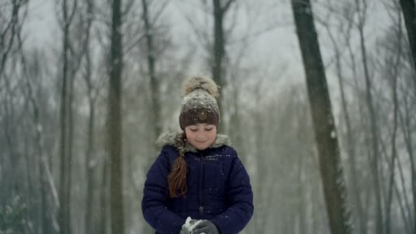 Kind speelt in de winter in het park gooit sneeuw op. Werpt sneeuwvlokken en glimlacht in een winterpark. Langzame beweging. Sluiten. — Stockvideo