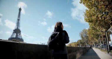 Sırt çantalı turist kız Paris 'te yürüyor, Eyfel Kulesi' ni ve Seine Nehri 'ni geçiyor ve akıllı telefondan fotoğraf çekiyor. Geniş açı