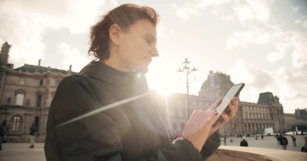 Mulher olha e tirar fotos com câmera de telefone em dia ensolarado fora em Paris França Europa. Tiro largo — Vídeo de Stock