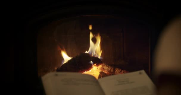 Slow Motion, vrouw die een boek leest bij de open haard. Ontspannen vakantie avond concept. wazig boek het boek wordt opgeheven — Stockvideo