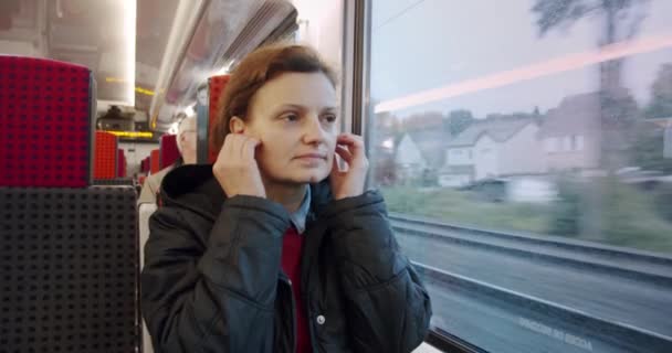 Mladá žena si nasadí sluchátka a poslouchá hudbu a prohlíží si mobilní telefon ve veřejné dopravě. Pomalý motiv — Stock video