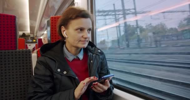 Ung kvinna i hörlurar lyssnar på musik och surfar på mobiltelefon ridning i kollektivtrafik. Långsam motin — Stockvideo