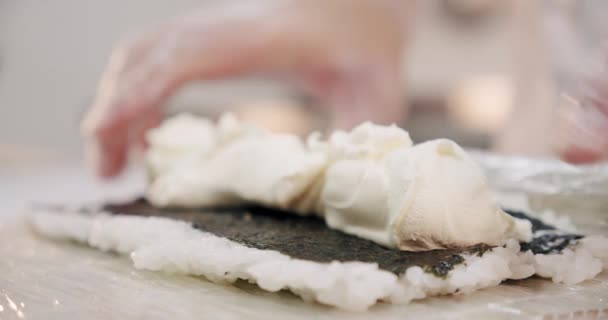 Cozinha de restaurante. O chef de sushi masculino prepara rolos de sushi japoneses de arroz, salmão, abacate, queijo e nori. Mãos fechadas . — Vídeo de Stock