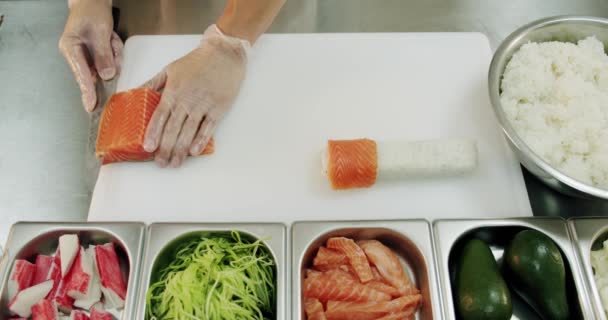 Cocina del restaurante. Chef de sushi masculino prepara rollos de sushi japonés de arroz, salmón, aguacate y nori. Vista superior — Vídeos de Stock