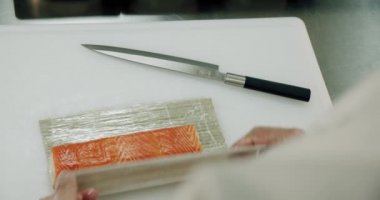 Restoran mutfağı. Erkek suşi şefi Japon suşi ruloları pilav, somon, avokado ve nori hazırlıyor. Suşi üst görünümünü döndürür