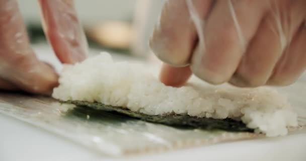 レストランキッチン。男性の手寿司職人は、米、サーモン、アボカド、海苔の日本の寿司ロールを準備します。閉鎖だ. — ストック動画