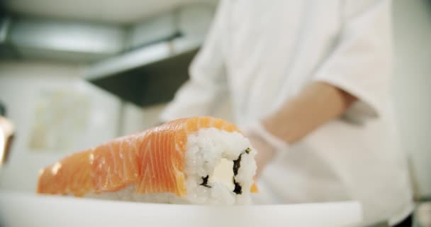 Κουζίνα εστιατορίου. Αρσενικό σεφ σούσι ετοιμάζει ιαπωνικά ρολά σούσι από ρύζι, σολομό, αβοκάντο και nori. — Αρχείο Βίντεο
