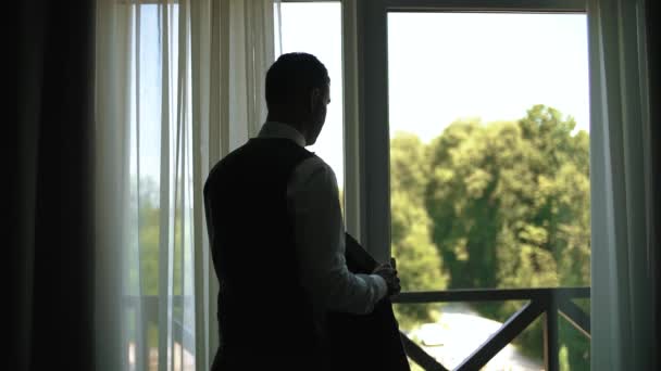 A silhueta de um homem usa um casaco em frente à janela. Movimento Sloe — Vídeo de Stock
