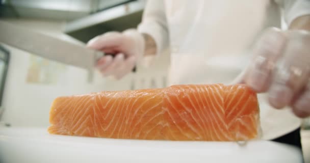 Kuchnia restauracji. Mężczyzna sushi szef kuchni przygotowuje japońskie sushi rolki ryżu, łososia, awokado i nori. kroi gotowe sushi na kawałki — Wideo stockowe