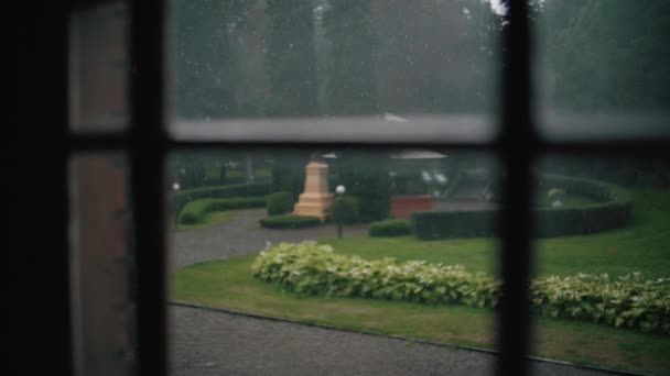 Lluvia en cámara lenta sobre vidrio de ventana con árboles verdes afuera . — Vídeos de Stock