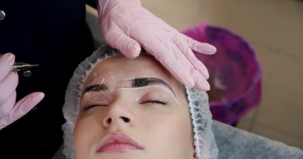 The cosmetologist begins the procedure correction the shape of eyebrows in a beauty parlor. A method of eyebrow correction with powder spraying. Microblading, eyebrow tattoo,. Slow motion — ストック動画