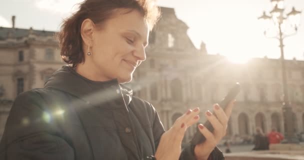 Mujer mira y tomar fotos con la cámara del teléfono en el día soleado en el casco antiguo. Primer plano. — Vídeo de stock