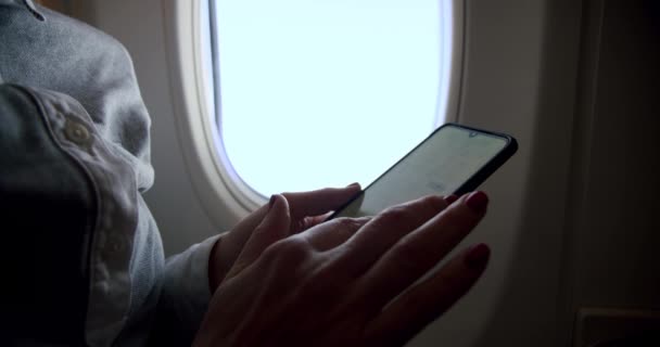 Increíble foto de una joven mujer relajada sosteniendo un teléfono inteligente en el asiento de la ventana soleado vuelo del avión. Primer plano en cámara lenta — Vídeo de stock
