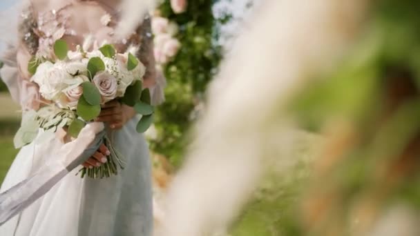 Mariée tient bouquet dans ses mains, rubans se déroulent dans le vent. Au ralenti. Gros plan — Video