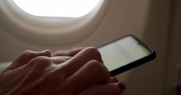 Primer plano increíble disparo de la joven mujer relajada sosteniendo un teléfono inteligente en el vuelo del avión asiento de la ventana soleado. Movimiento lento — Vídeo de stock