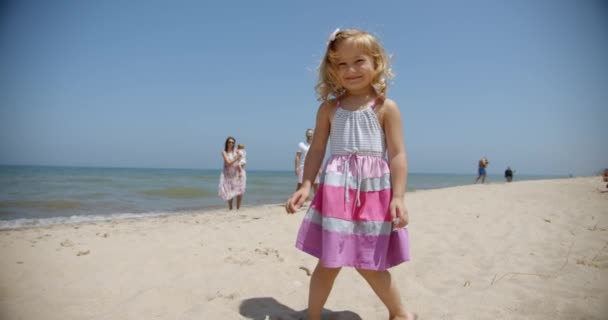 Criança pequena feliz correndo para seu pai abraçando na praia de outono no fundo fica mãe com bebê em seus braços. Happy Childhood câmera lenta — Vídeo de Stock