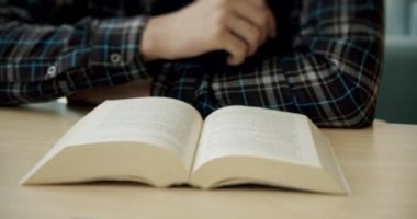 Üniversite öğrencisi kütüphanede oturuyor, kitabı okuyor ve sayfaları çeviriyor. Kapat.