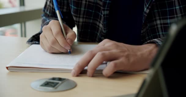 Egyetemi hallgató ül a könyvtárban, ír egy notebook, közelről — Stock videók