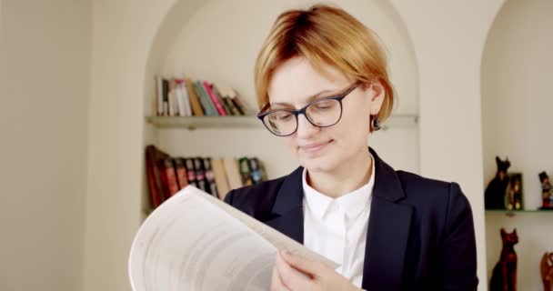 Retrato mujer empresaria exitosa en traje de negocios negro y gafas con un libro en sus manos en la oficina. Mirando a la cámara — Vídeo de stock