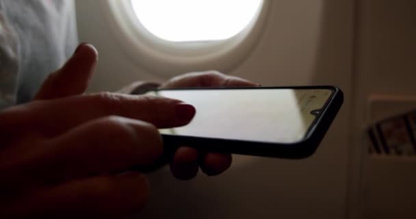 Gros plan d'une femme tenant un téléphone intelligent sur un siège de fenêtre ensoleillé en vol d'avion. Mouvement lent — Video