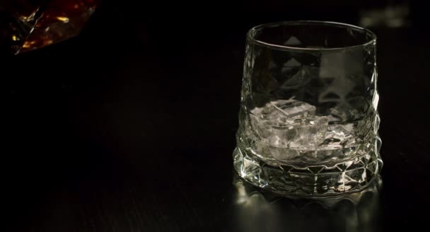 Повільний рух золотистого віскі вливається в склянку з кубиками льоду з пляшки. крупним планом — стокове відео