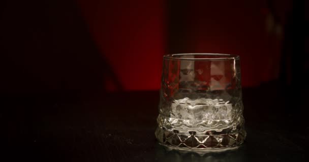 Slow motion gyllene whisky häller i glaset med isbitar från flaskan på en röd bakgrund. Närbild — Stockvideo