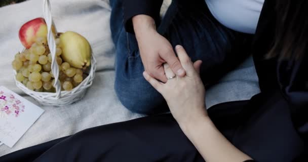 Hombre y mujer tomados de la mano con anillos de boda sentados en cuadros con canasta de frutas — Vídeo de stock