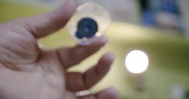 Ik maak glazen. De oogarts houdt de afgewerkte lens in zijn handen en onderzoekt deze in een optische winkel. Langzame beweging Close-up — Stockvideo