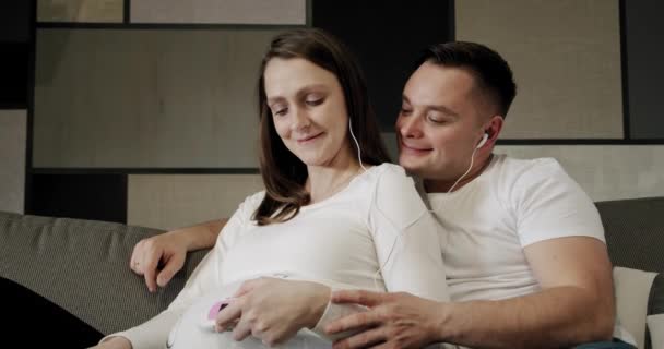 Glada unga par tillsammans i sängen, Leans och lyssnar på en baby flytta och dess hjärtslag i magen. — Stockvideo