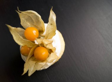 krem ve siyah bir zemin üzerine bir physalis ile cupcake