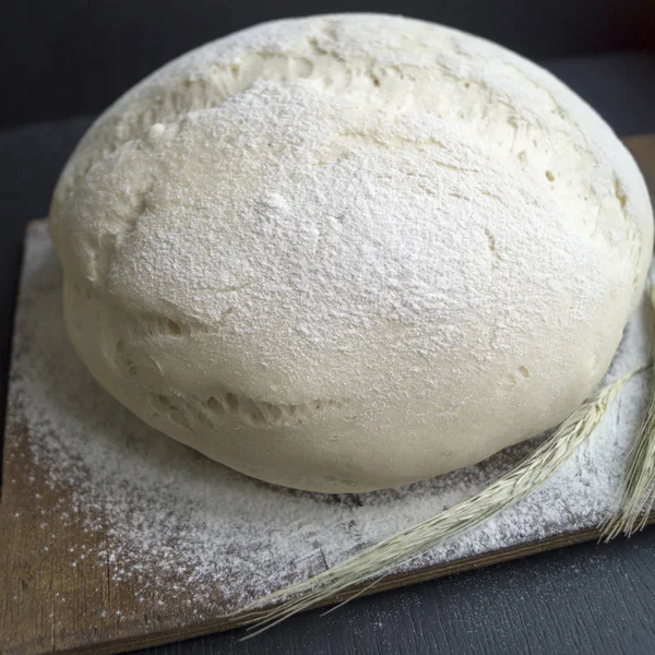 Una bola de masa de pizza sobre un tablero rústico de madera sobre fondo negro —  Fotos de Stock